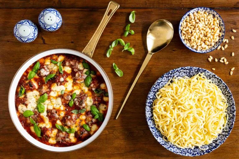 Basil chicken meatballs baked in tomato sauce with melted mozzarella and fresh basil, served with pasta on a wooden table.