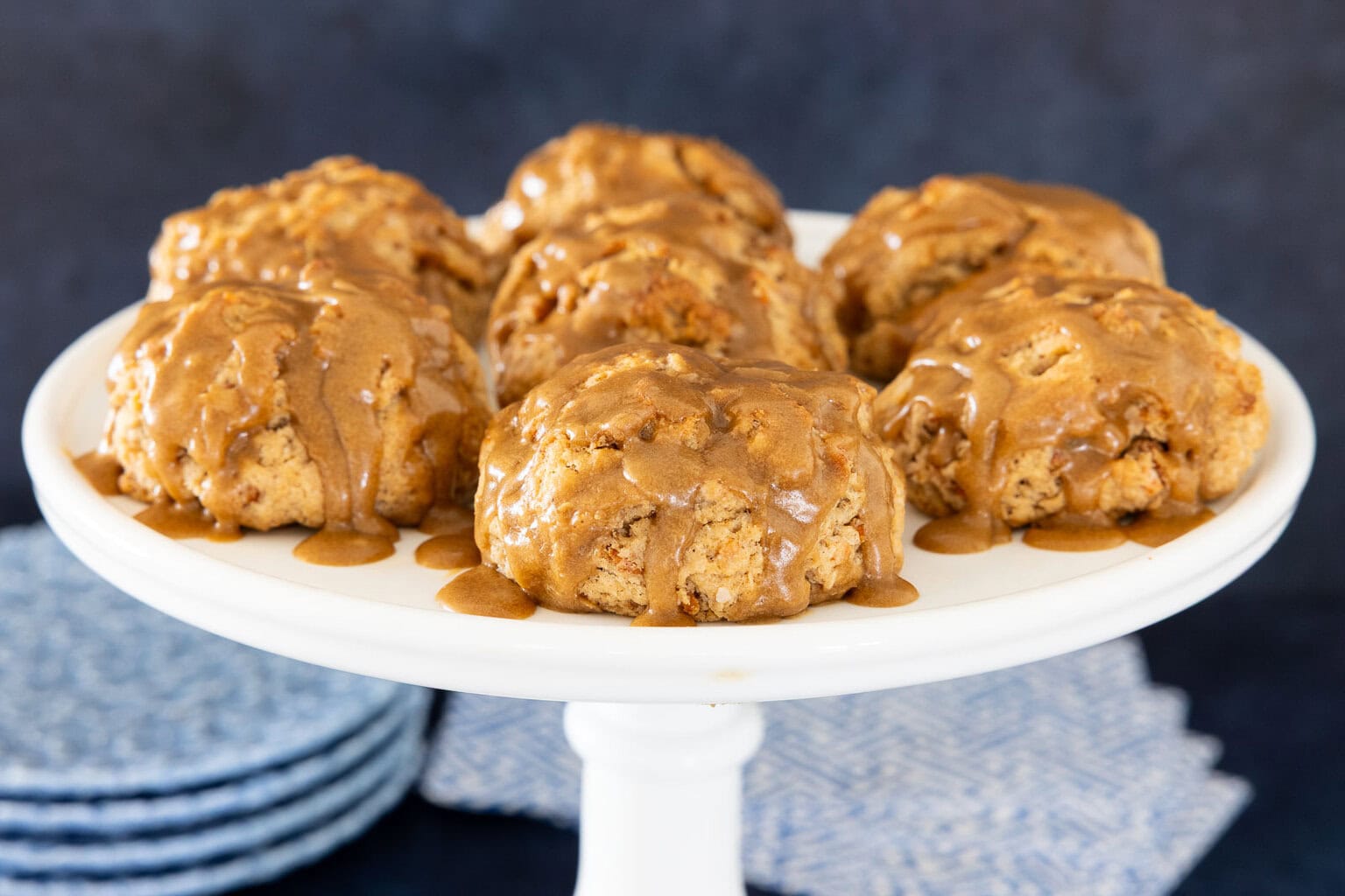 Carrot cake scones covered with brown sugar caramel glaze on a white cake stand