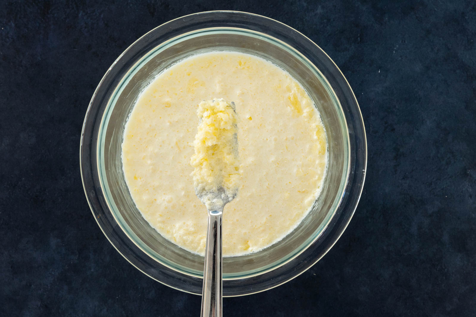 Melted butter and chilled heavy cream forming small butter globules in a glass bowl