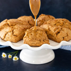 Carrot cake scone drizzled with brown sugar caramel glaze on a white cake stand