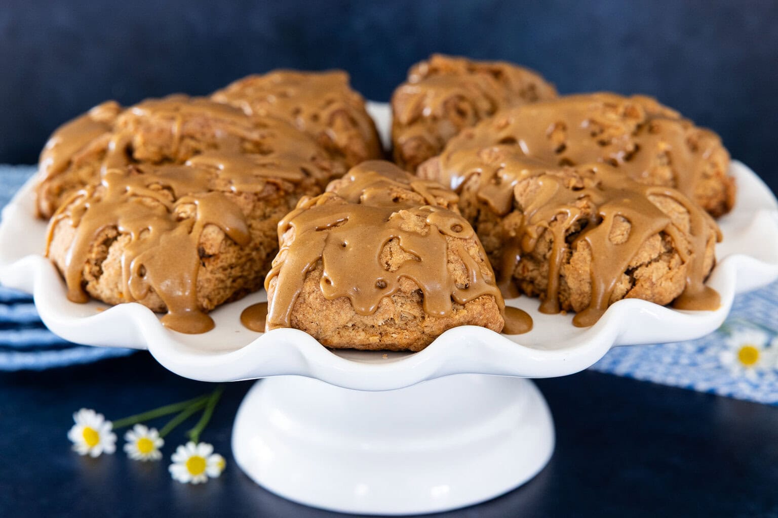Carrot cake scones topped with brown sugar caramel glaze on a white cake stand