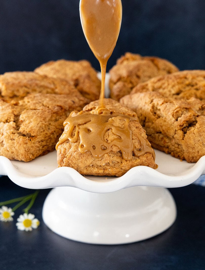 Carrot cake scone drizzled with brown sugar caramel glaze on a white cake stand