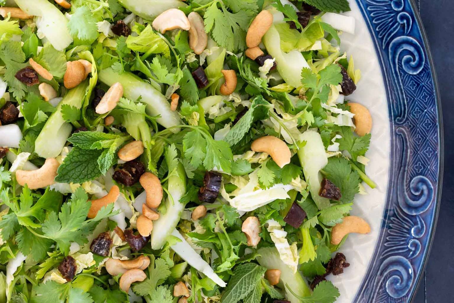 Close-up of Asian celery date salad with herbs, cabbage, dates and cashews on platter.
