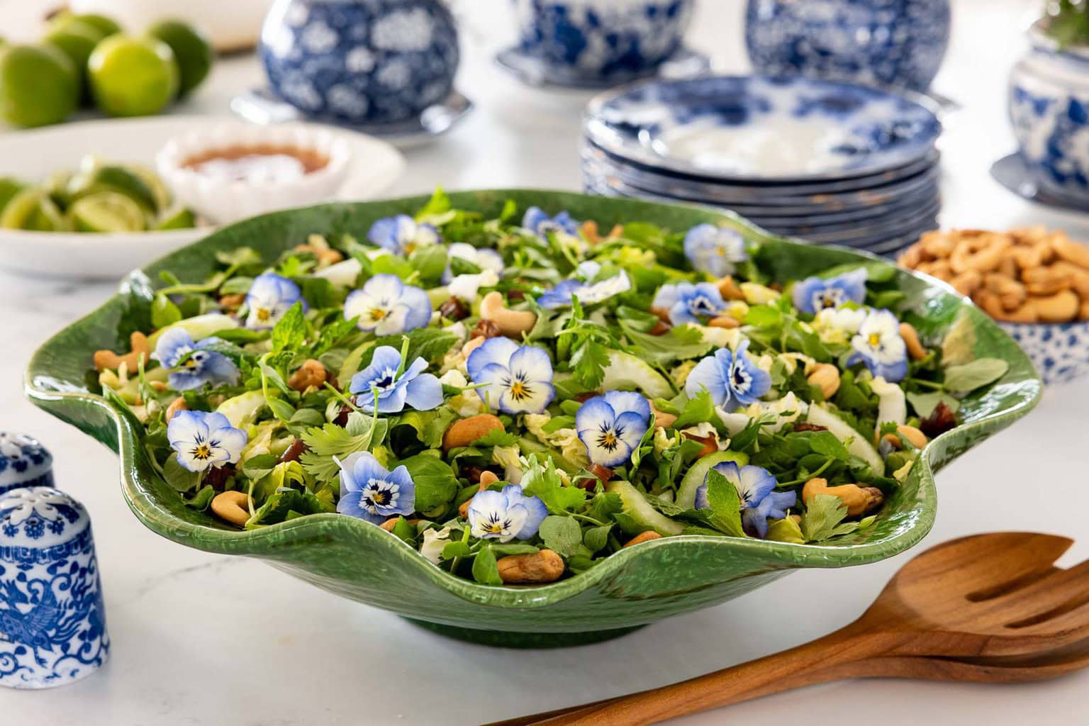 Asian celery date salad with herbs, cashews and edible flowers served in a green bowl.