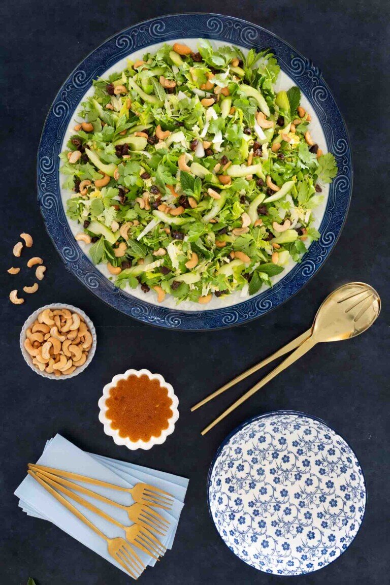 Asian Date Salad in a blue bowl with dressing, cashews and blue and white plates.