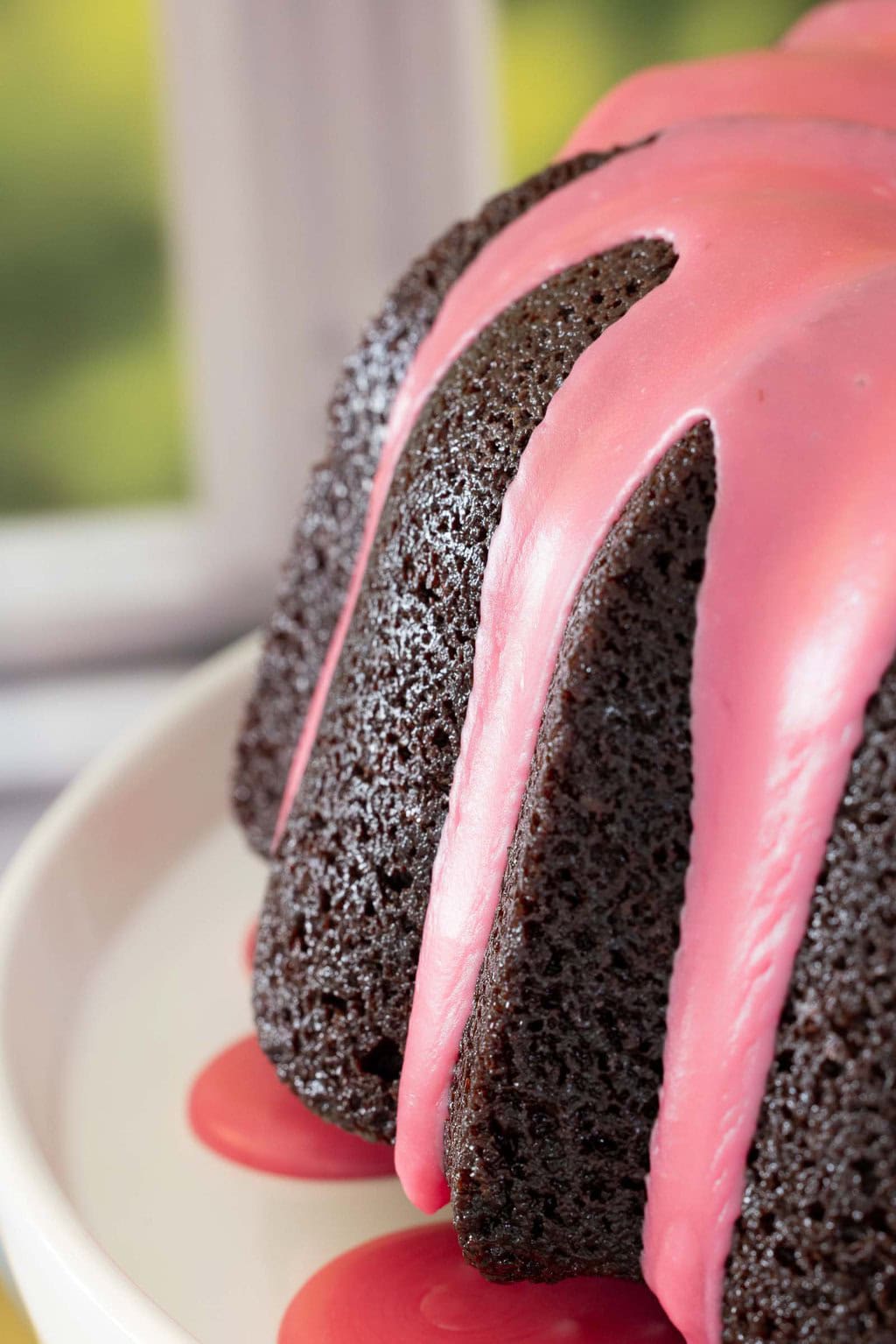 Close-up of chocolate pound cake with fresh strawberry icing dripping down the sides.
