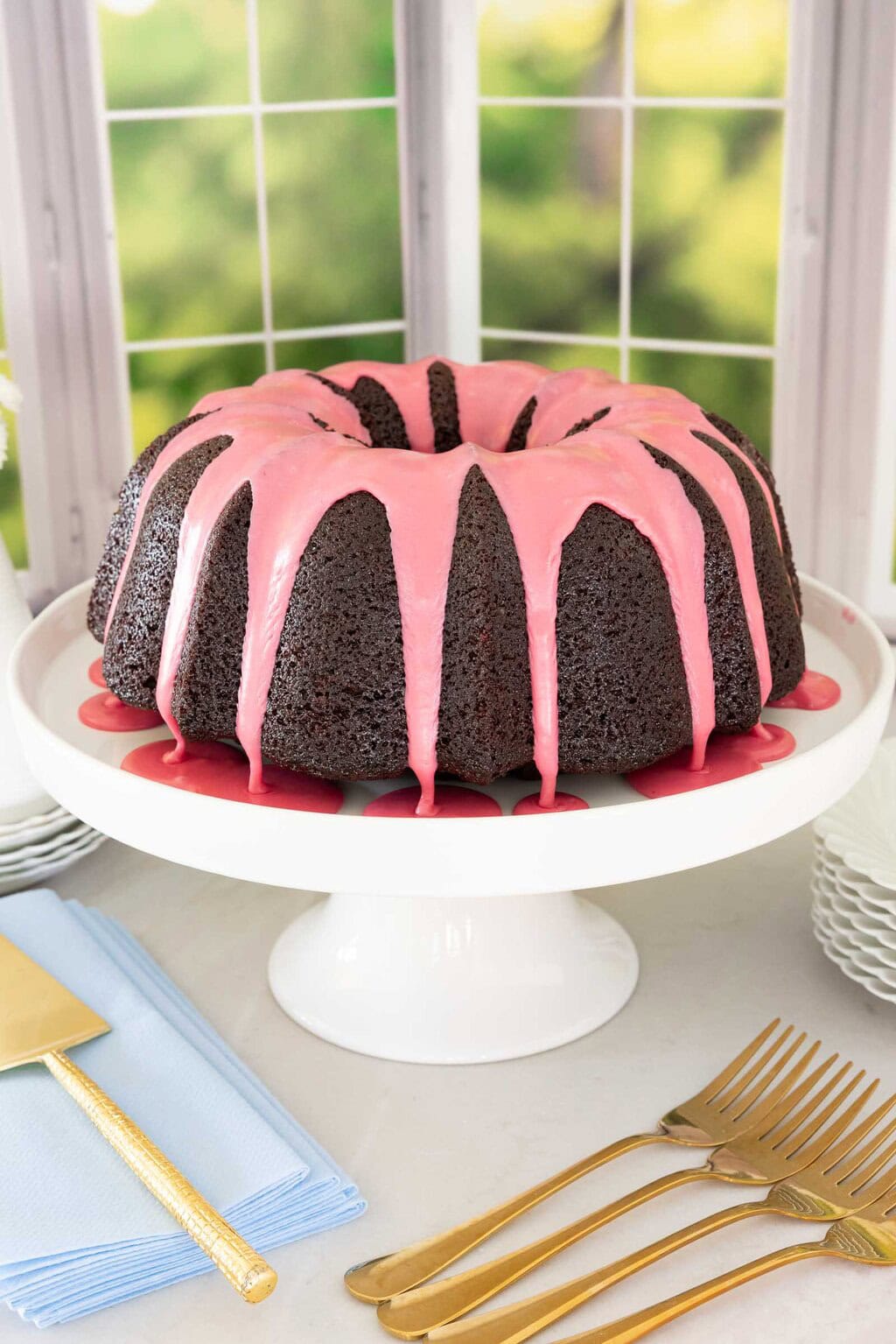 Chocolate pound cake with fresh strawberry icing dripping down the sides on a white cake stand.