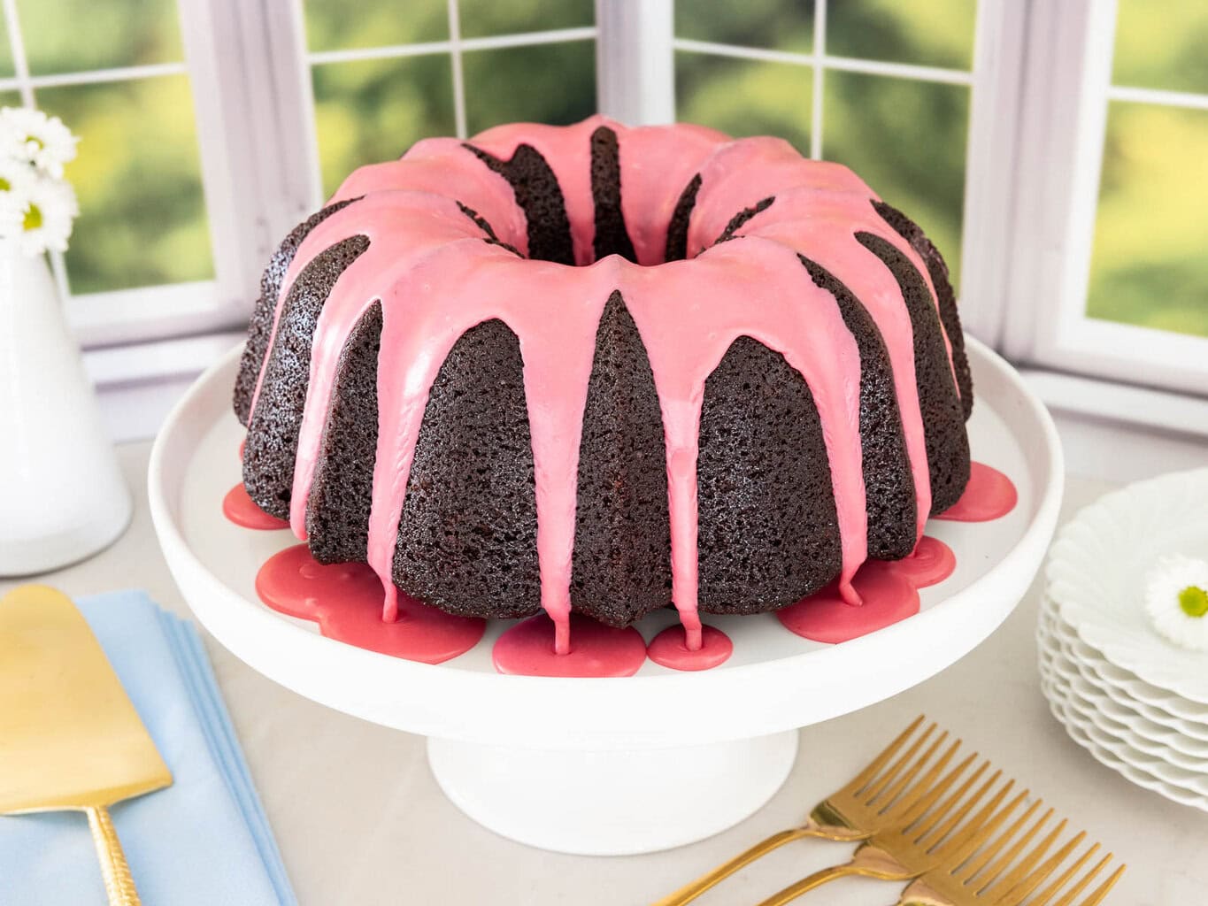 Chocolate pound cake with fresh strawberry icing dripping down the sides on a white cake stand.