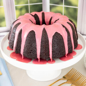 Chocolate pound cake with fresh strawberry icing on a white cake stand with pink glaze dripping down the sides.