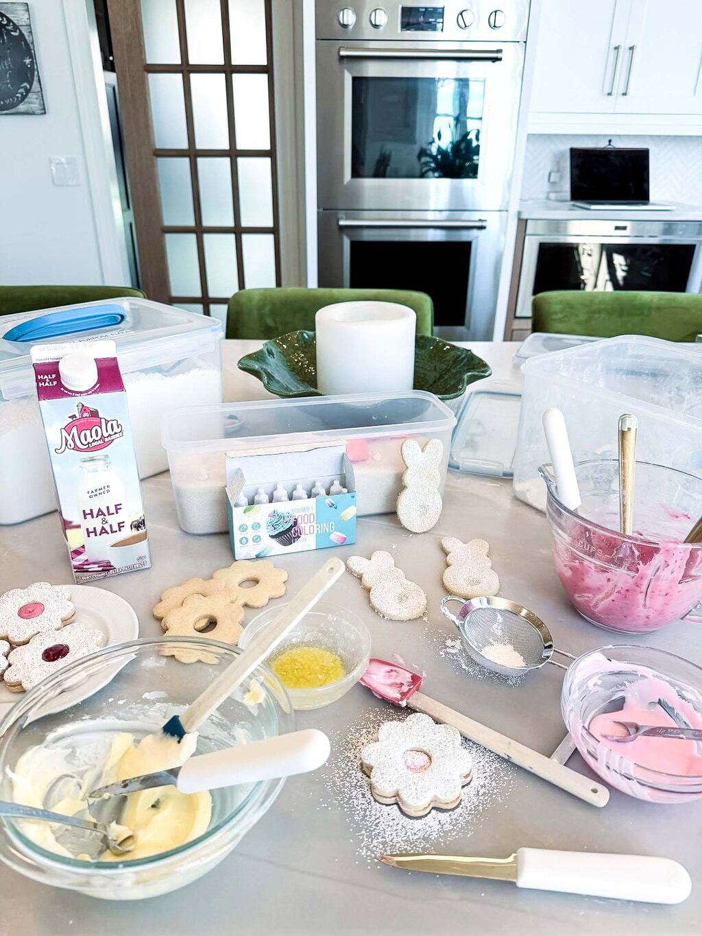 Messy kitchen counter with bowls of icing, shortbread cookies, sprinkles and baking ingredients while making Easter cookies