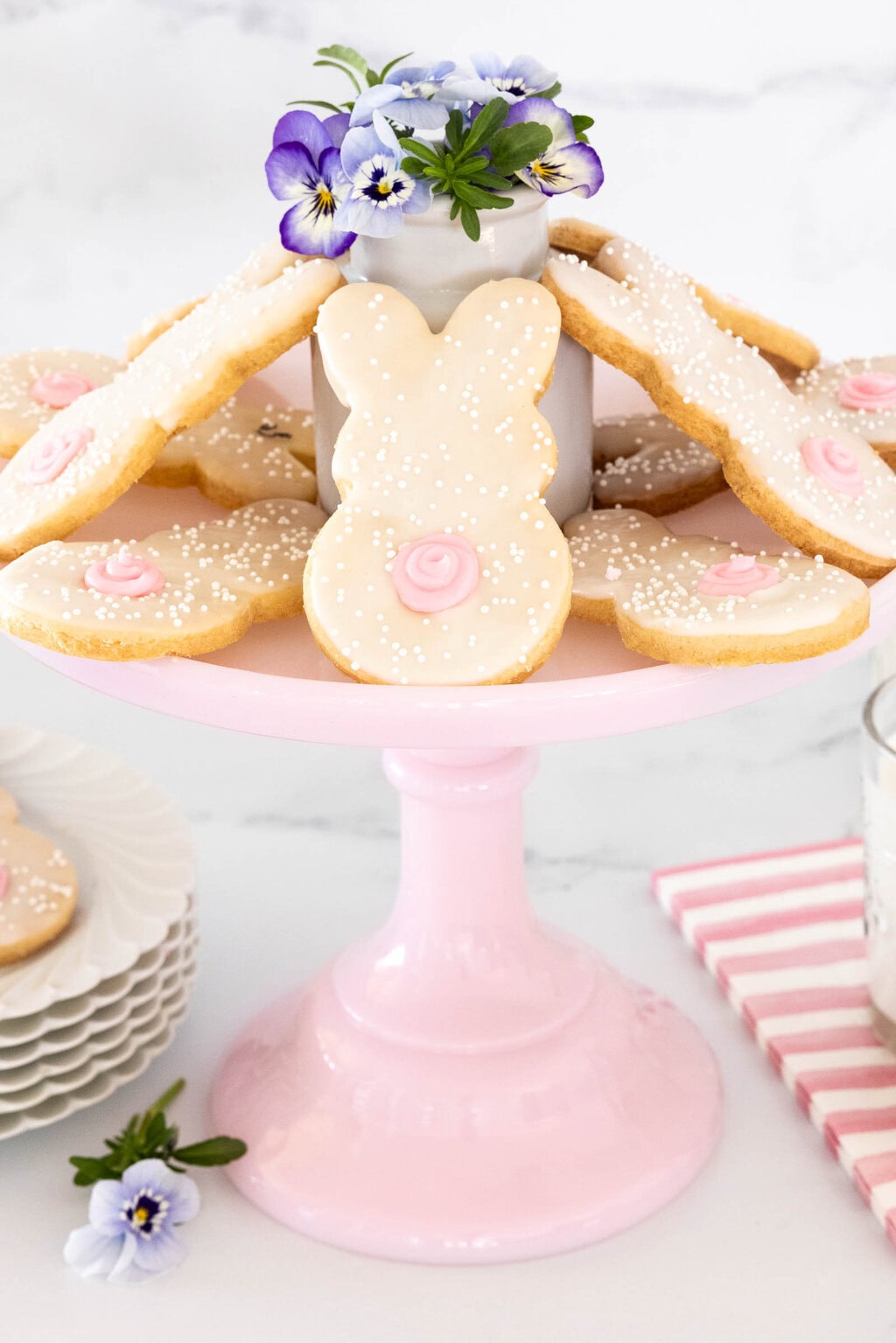 Easter bunny shortbread cookies with white icing and pink details displayed on a pink cake stand with spring flowers