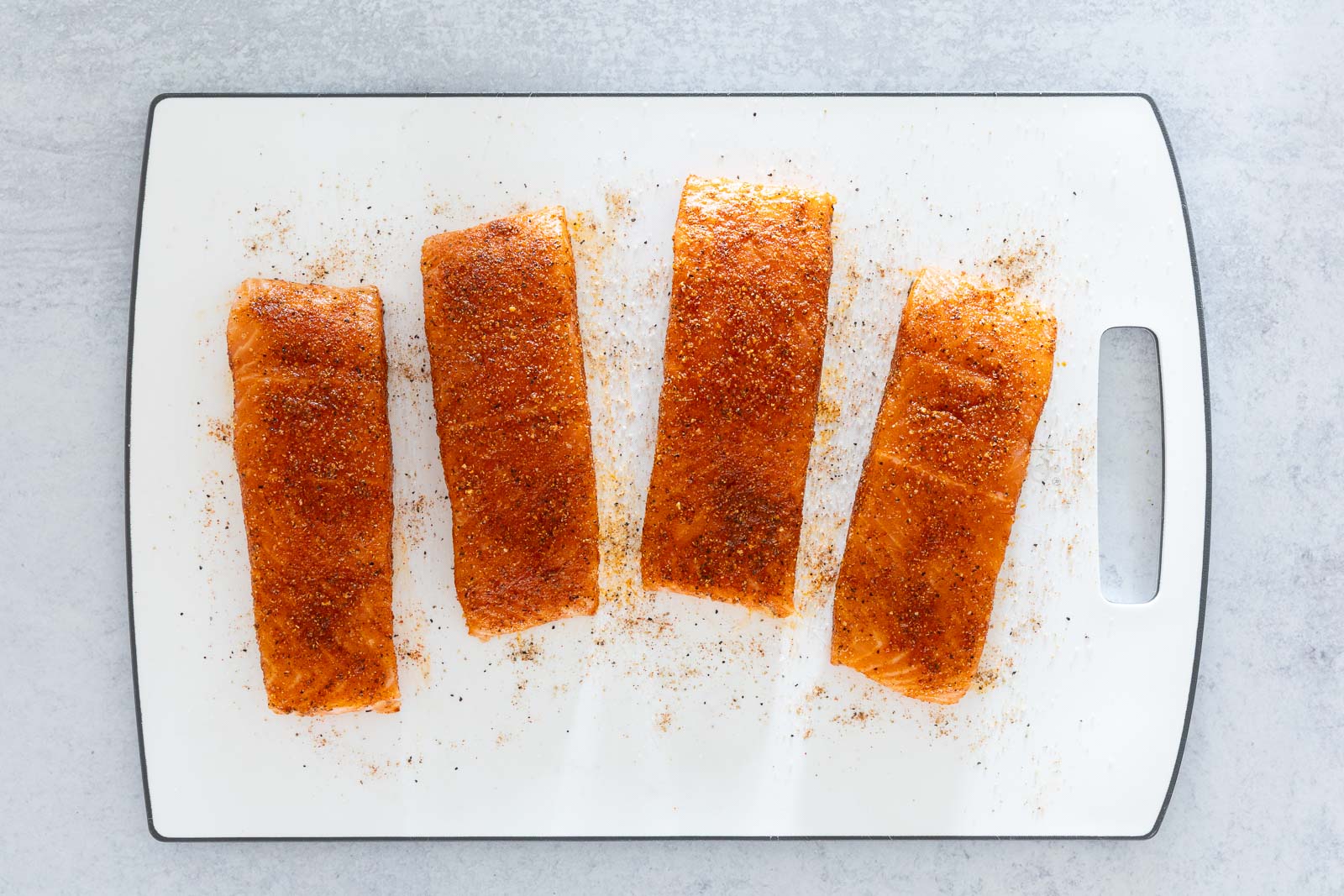 Salmon fillets coated with a spice rub on a cutting board before cooking pan-seared salmon.