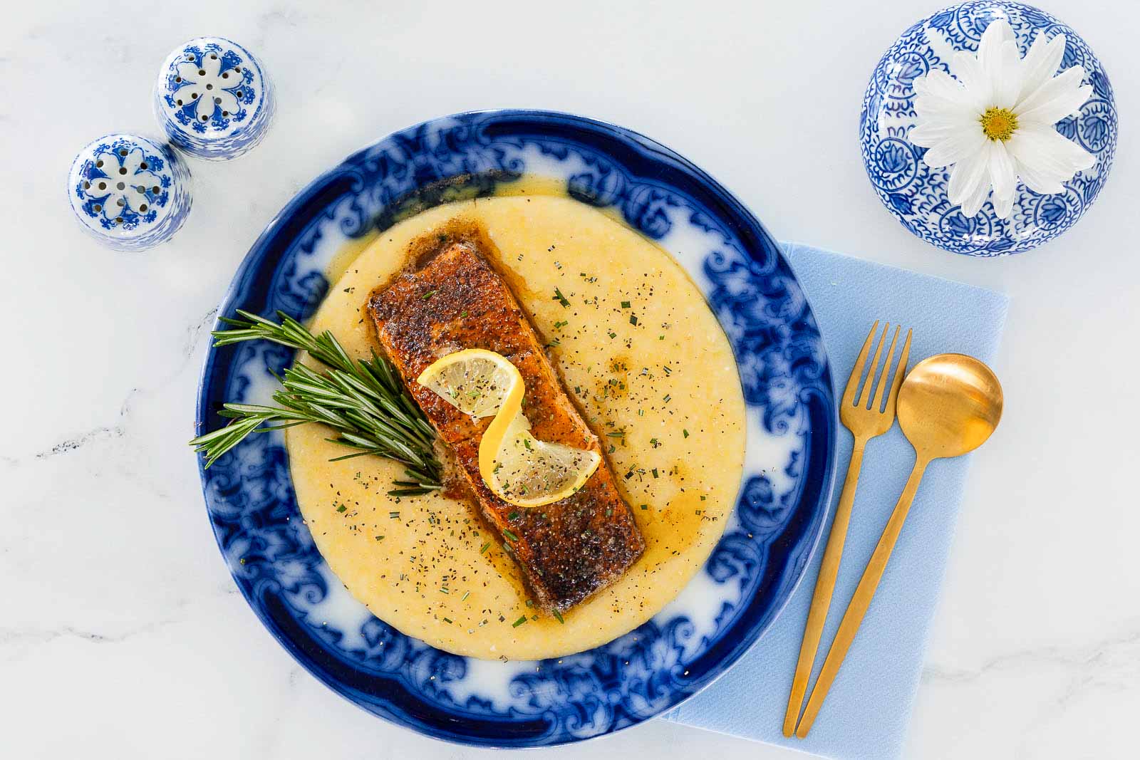Pan-seared salmon served over creamy polenta with lemon slices and rosemary on a blue plate.