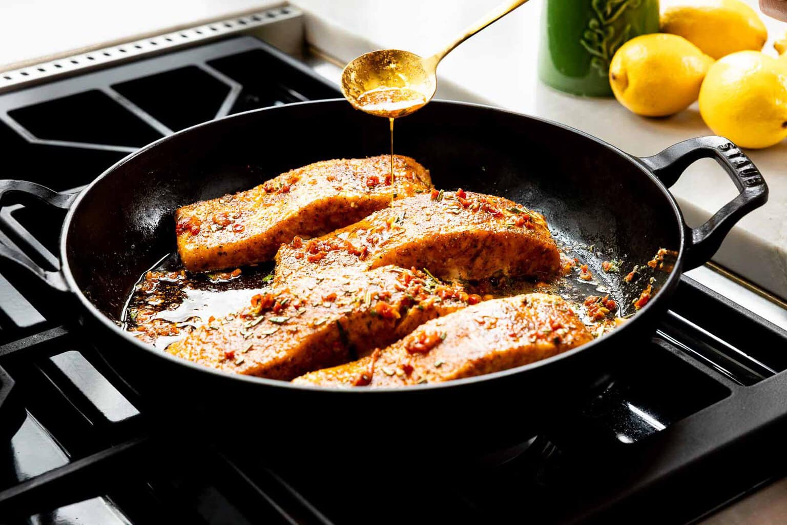 Pan-seared salmon fillets in a skillet being basted with garlic herb butter and sun-dried tomatoes.
Pan-searing salmon in a hot skillet helps create a golden crust while keeping the inside tender and flaky, and basting the fish with butter adds both flavor and moisture as it cooks.