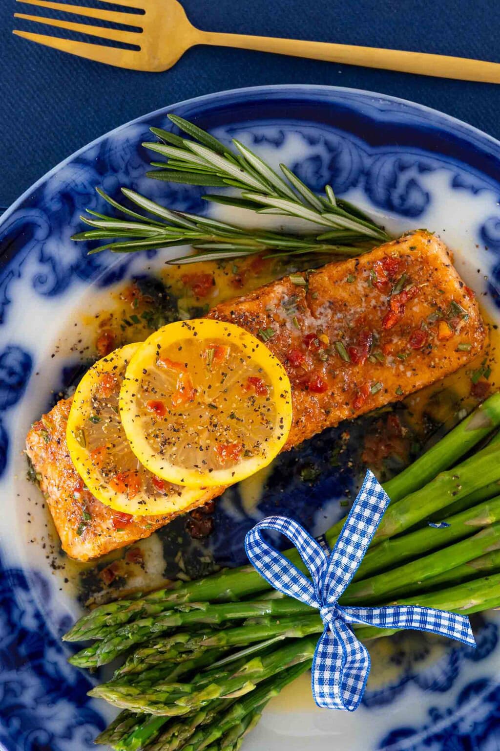 Italian Garlic Butter Salmon on a blue and white plate with a bundle of asparagus tied with blue and white ribbon.