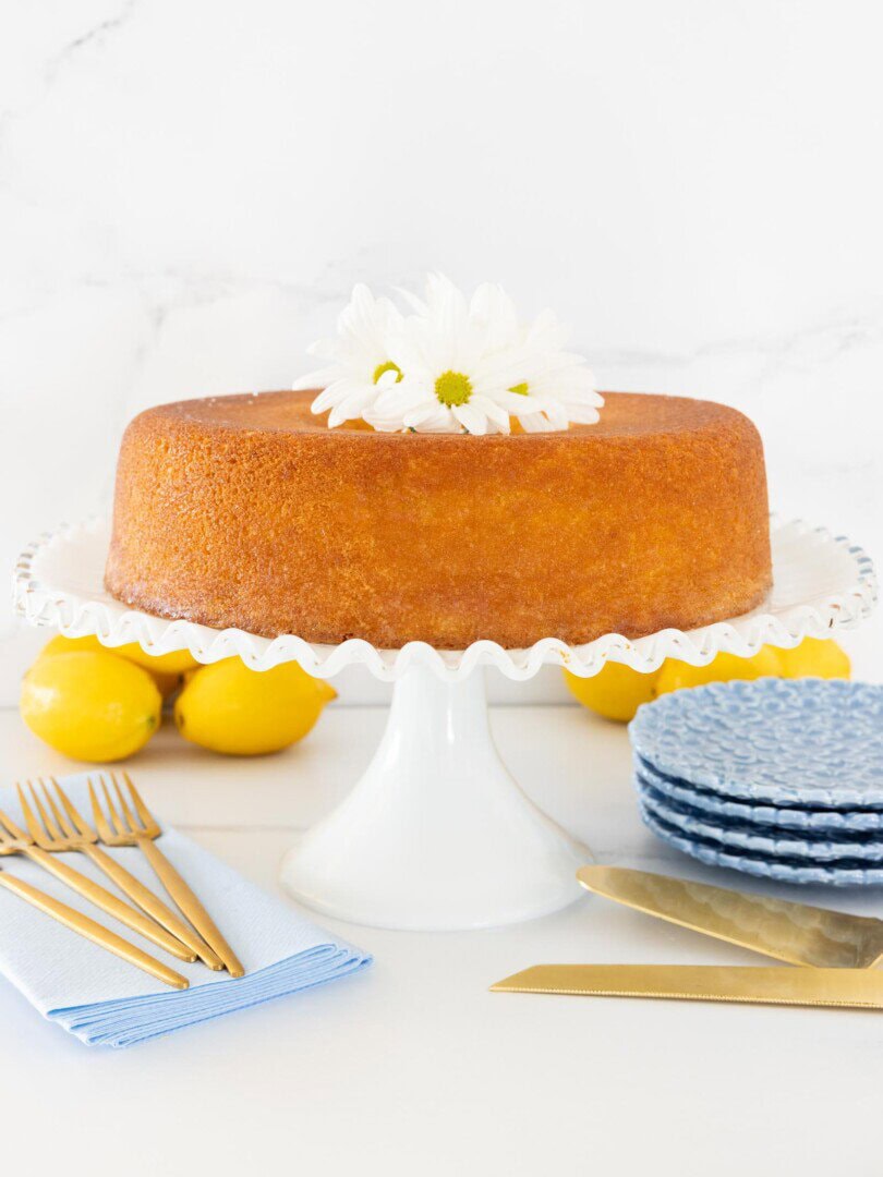 Italian Olive Oil Bundt Cake on a white cake stand with blue plates and lemons in the background.