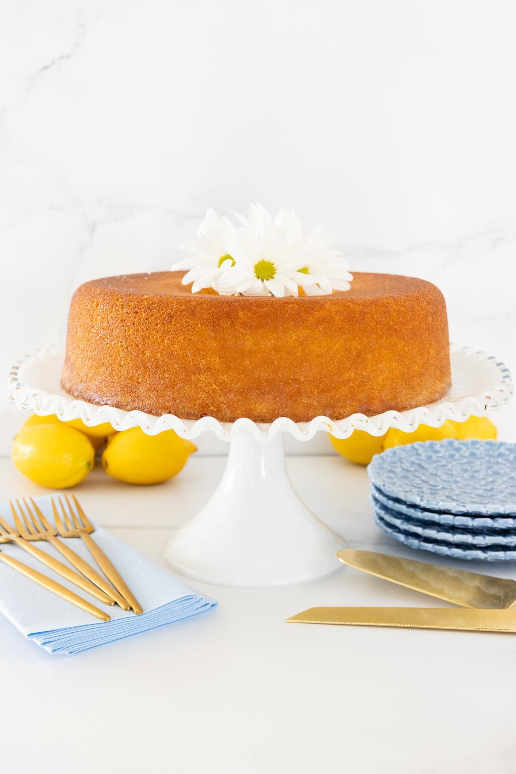 Italian Olive Oil Bundt Cake on a white cake stand with blue plates and lemons in the background.