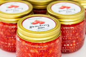 Several small glass jars filled with homemade strawberry freezer jam and topped with gold lids and strawberry labels.