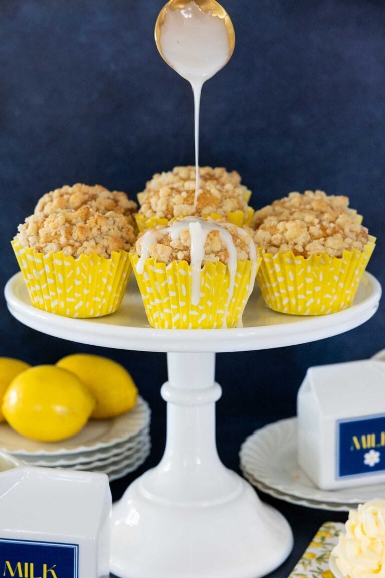Lemon Crumble muffins on a white cake stand with icing drizzled on top.