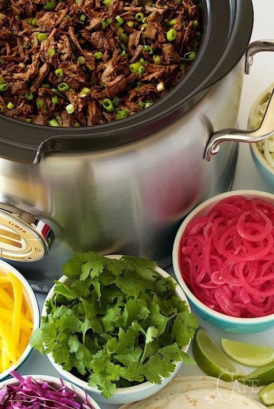 Mexican Shredded Beef in a slow cooker with small bowls of toppings.