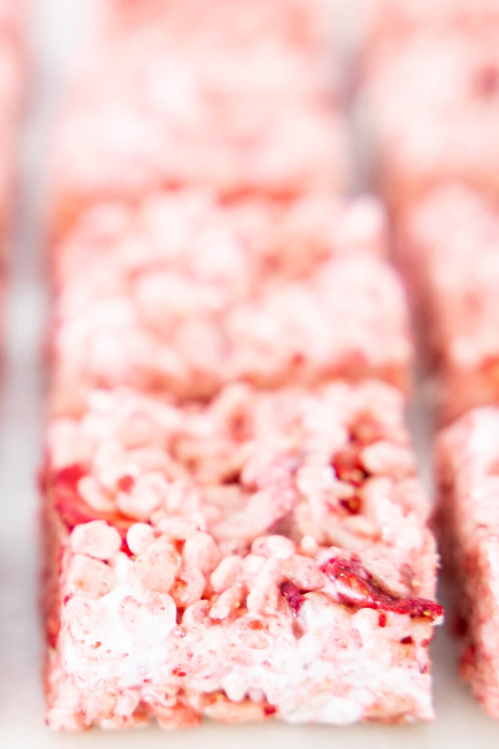 Close-up of strawberry rice krispie treat square showing gooey marshmallow texture and pieces of freeze-dried strawberries