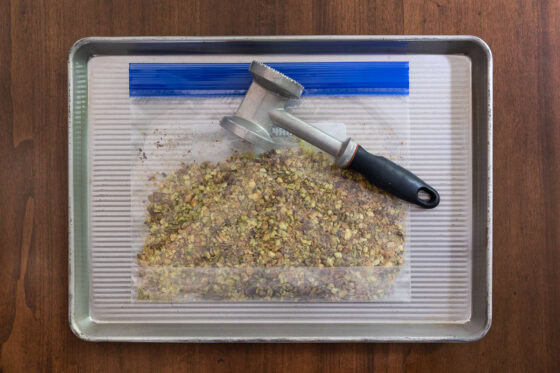 Shelled pistachios crushed in a zip-top bag with a meat mallet on a sheet pan for making Maple Pistachio Brittle.