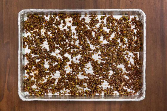 Overhead view of Maple Pistachio Brittle mixture spread in a thin layer on a foil-lined baking sheet before baking.