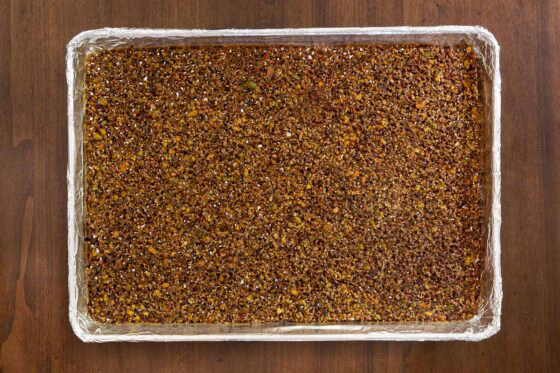 Overhead view of Maple Pistachio Brittle cooling on a foil-lined baking sheet after baking, before breaking into crunchy shards.