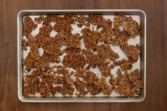 Overhead view of crunchy Maple Pistachio Brittle broken into crisp golden shards on a sheet pan after cooling.