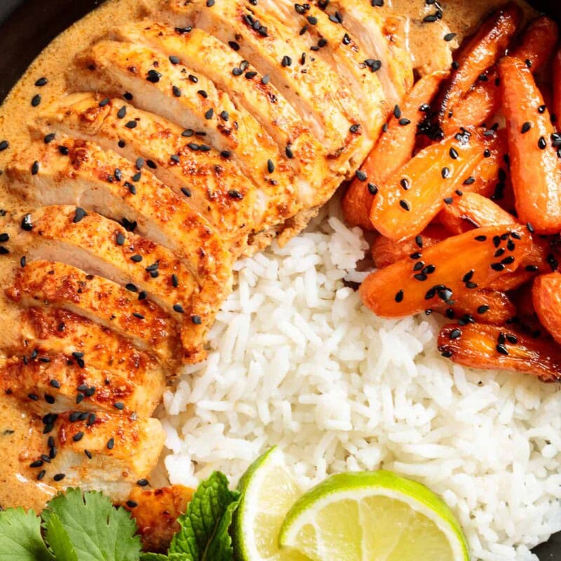 Coconut Braised Chicken Breasts, sliced in a black bowl with rice and roasted carrots.