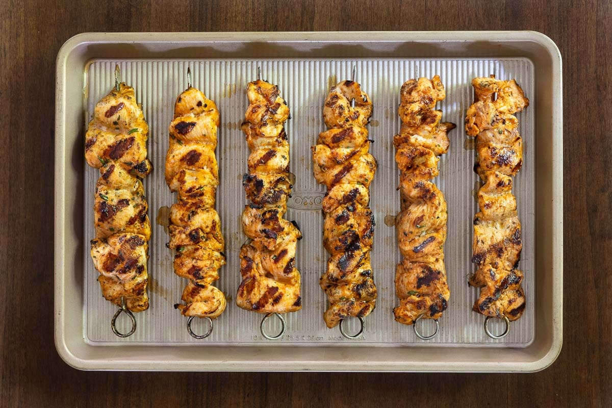 Cooked Italian chicken skewers with grill marks arranged on a sheet pan after grilling, showing juicy, golden-brown chicken marinated with Italian herbs and seasonings.