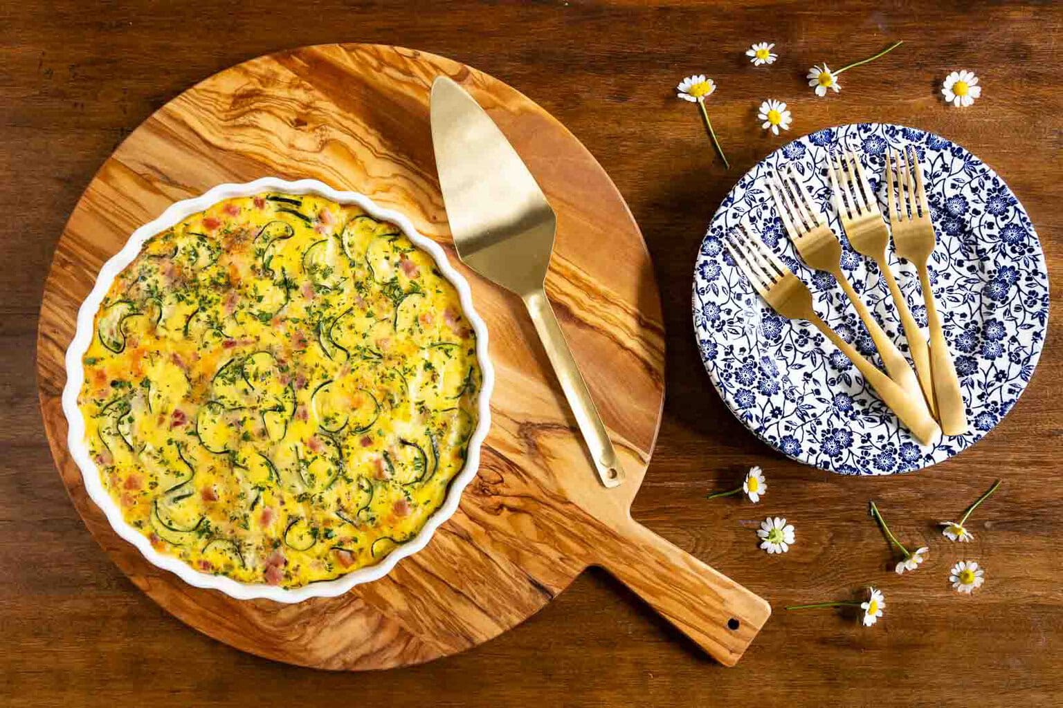 Southwestern ham and zucchini quiche in a white fluted dish with slices cut and one served on a blue patterned plate on a wooden table