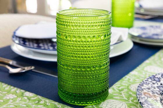 Bright green textured drinking glass on a spring table setting with blue placemats, blue and white dishes and a green floral tablecloth.