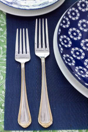 Blue and white floral dinner plate with white napkin, silver flatware, navy placemat and green glass on an elegant spring tablescape.