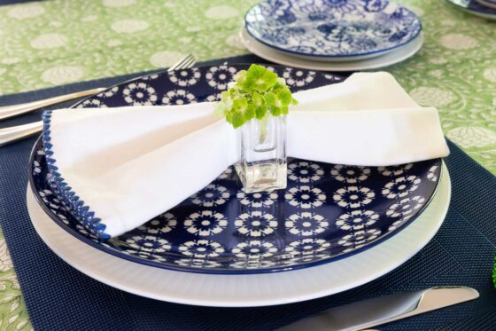 Blue and white floral dinner plate with folded white napkin and small green flower vase on an elegant spring and summer tablescape.