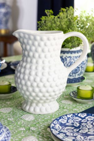 White hobnail pitcher on a blue and white spring tablescape with green candles, herb centerpieces and patterned dishes.