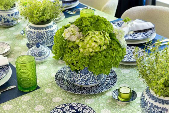 Green hydrangea centerpiece in a blue and white ceramic bowl on a spring and summer tablescape with patterned dishes, green glassware and fresh herb centerpieces.