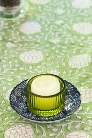 Green glass tealight candle holder on a blue plate with a green and white patterned tablecloth and elegant spring tablescape decor.