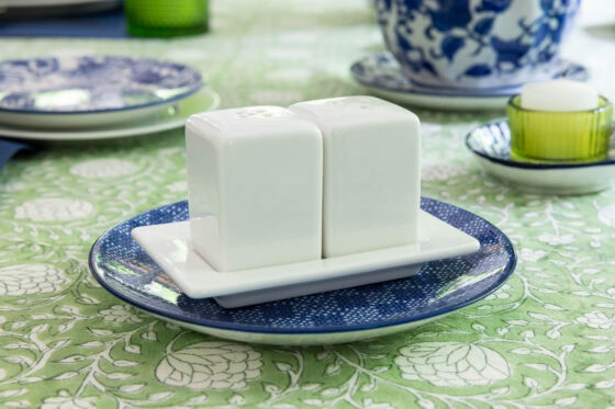 Simple white ceramic salt and pepper shakers on a blue plate with a green and blue spring tablescape in the background.