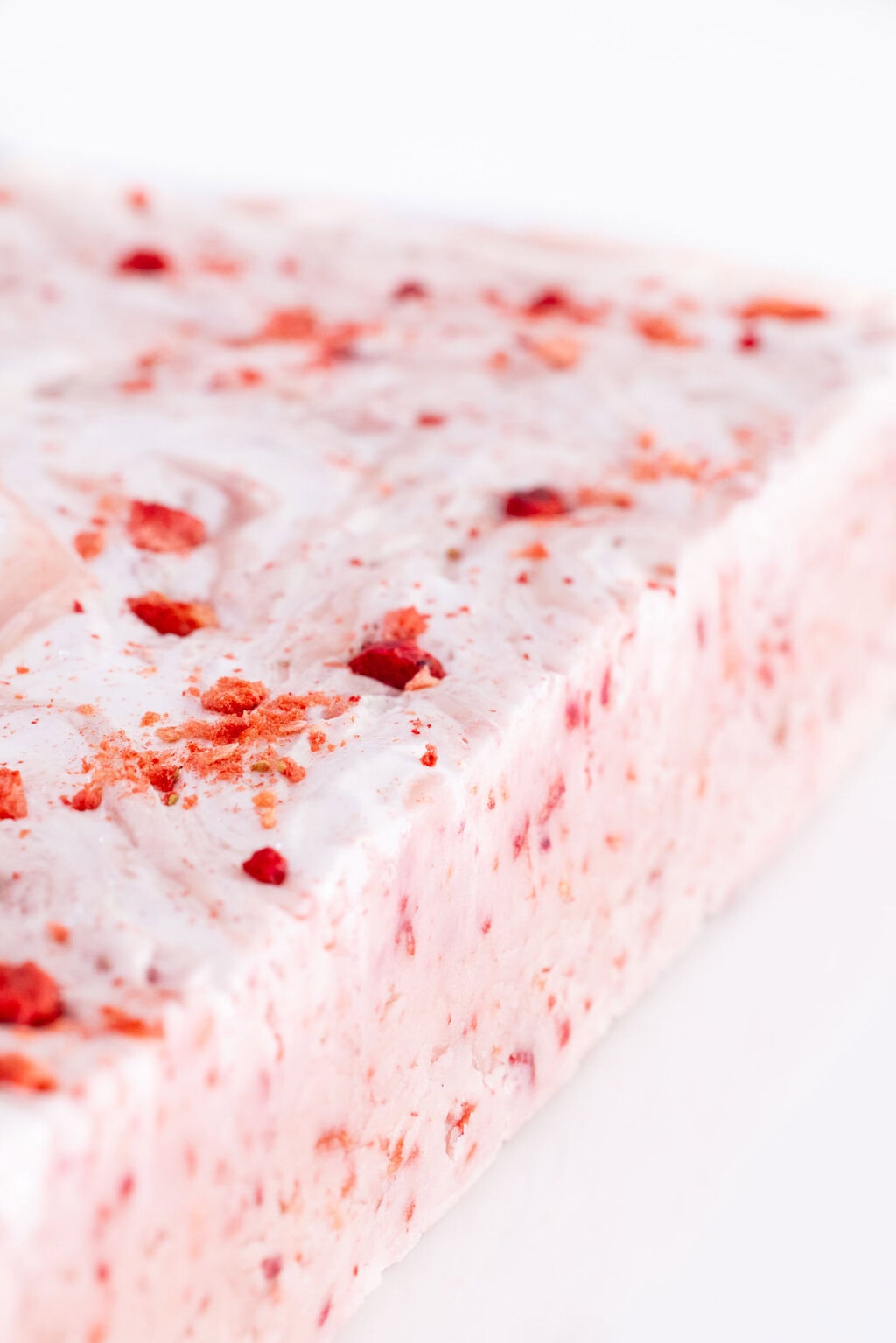 Close side view of homemade Strawberries & Cream Fudge topped with crushed freeze-dried strawberries, showing the creamy texture and strawberry pieces throughout the fudge.