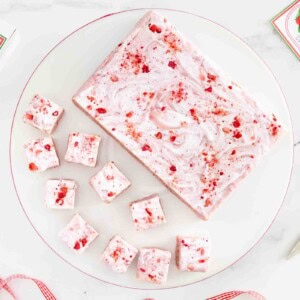 Overhead view of homemade Strawberries & Cream Fudge with swirls of marshmallow creme and crushed freeze-dried strawberries, surrounded by fudge squares and free printable gift labels on a white marble surface.