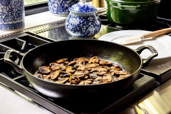 Golden brown crimini mushrooms sautéing in a cast iron skillet for One-Pan Balsamic Rosemary Chicken.