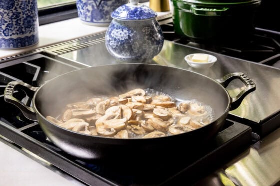 Sliced crimini mushrooms simmering in chicken broth in a cast iron skillet for One-Pan Balsamic Rosemary Chicken.