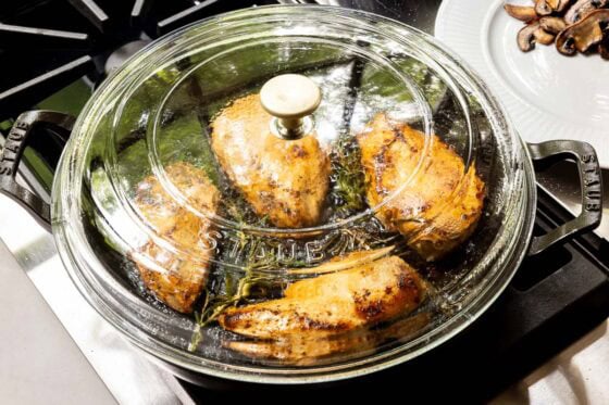 Chicken breasts finishing cooking under a covered skillet with fresh rosemary for One-Pan Balsamic Rosemary Chicken.