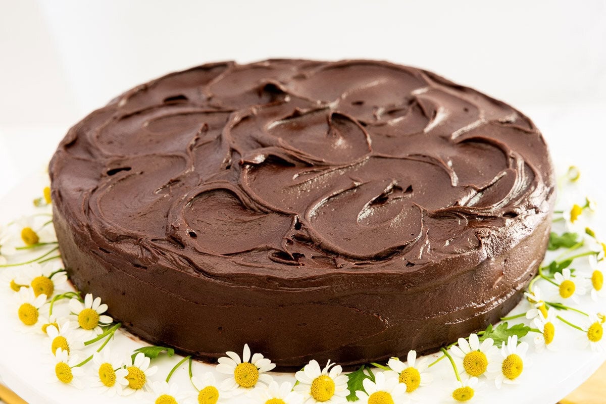 Whole Marry Me Italian Love Cake with chocolate frosting and chamomile flowers on a white cake stand.