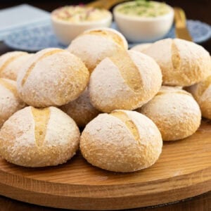 Basket-style arrangement of homemade no-knead Italian-style dinner rolls on a wooden serving board with compound butters in the background.