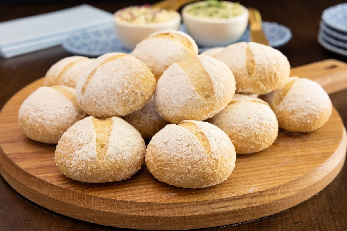 Close-up of homemade no-knead Italian-style dinner rolls on a wooden serving board with herb butter in the background.