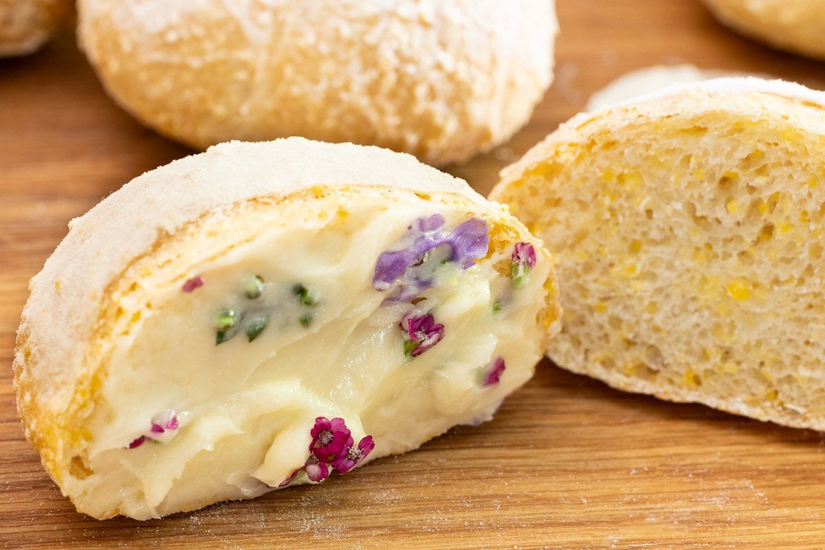 Close-up of a sliced no-knead Italian-style dinner roll spread with flower-topped compound butter, showing the tender, airy interior.