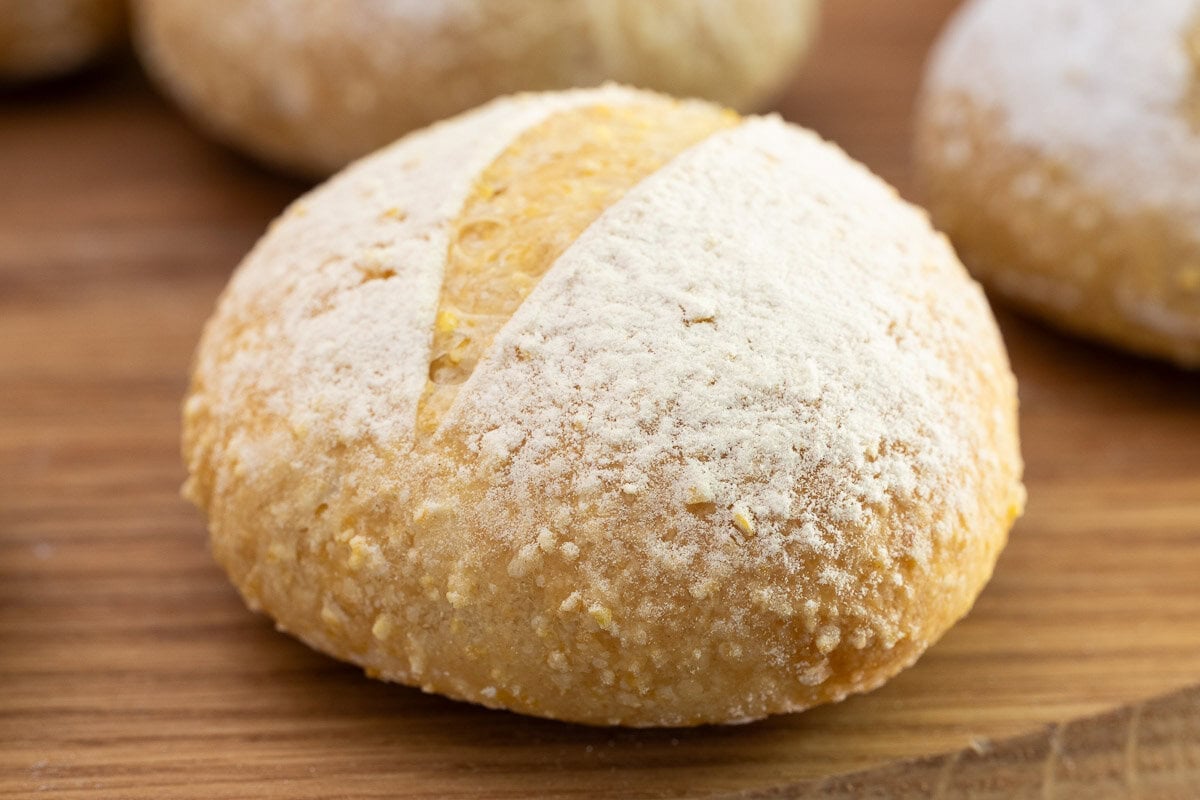 Close-up of a homemade no-knead Italian-style dinner roll with a flour-dusted crust and artisan-style score on a wooden board.