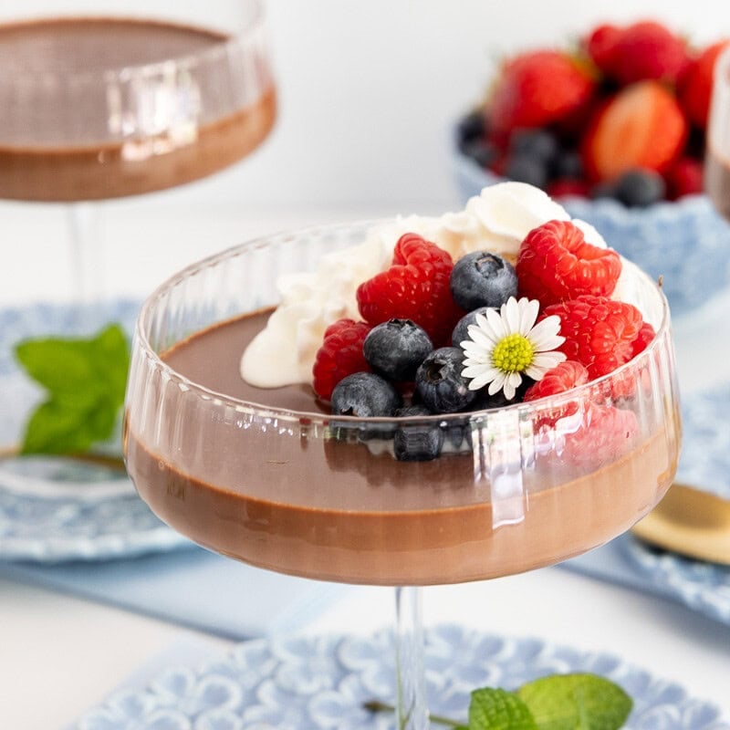 Chocolate panna cotta served in a glass dessert coupe and topped with whipped cream, fresh raspberries and blueberries.